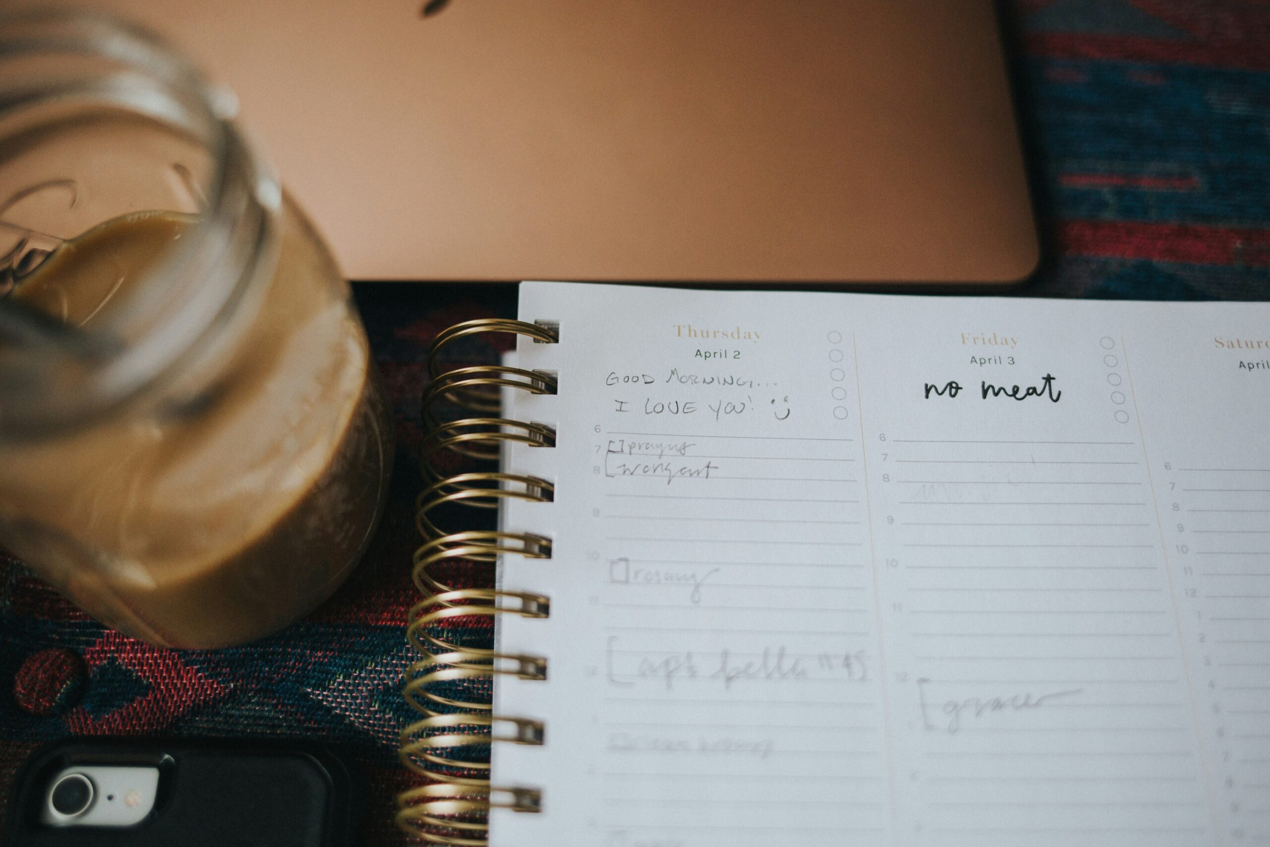 A weekly planner notebook open beside a coffee, used for jotting down the week's dinner plan