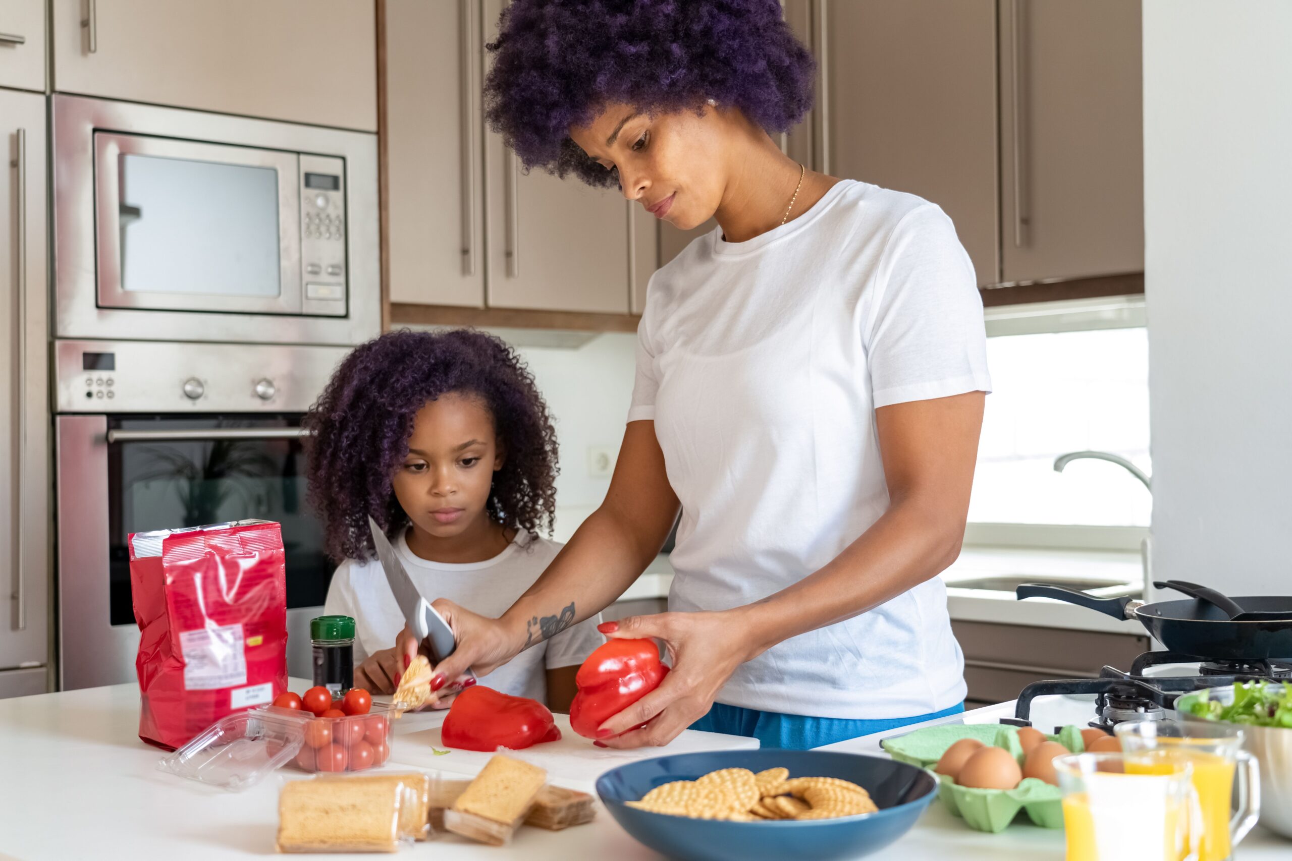 A mom and her child chopping vegetables together in the kitchen while making dinner