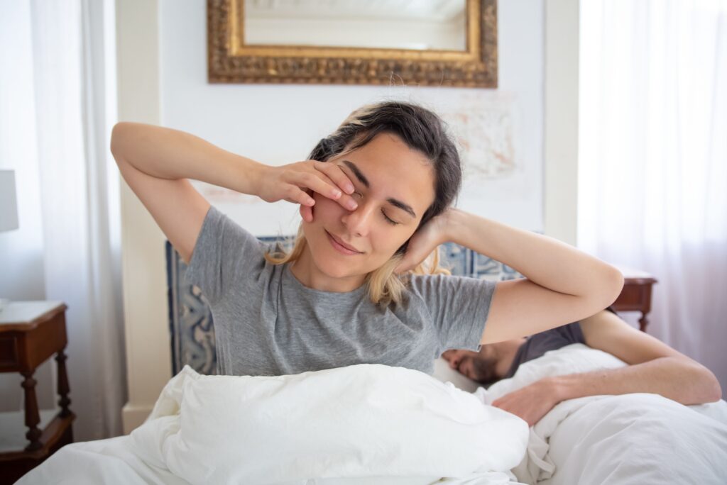 Woman waking up and stretching in a bright bedroom